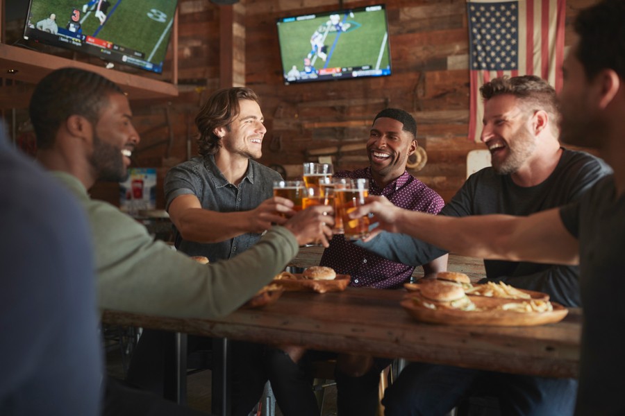 Four men sitting around a restaurant table, toasting to one another, holding beer glasses.