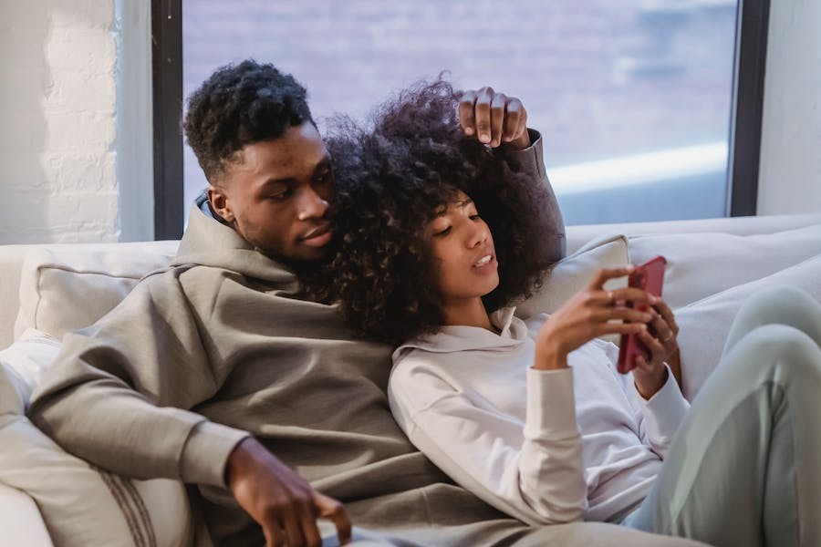 A couple sitting on the couch, relaxing and looking at a smartphone.